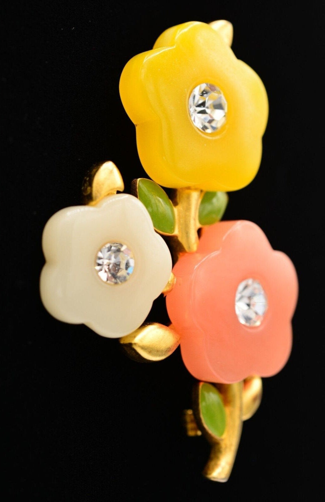 Side view of a vintage Givenchy brushed gold floral brooch with yellow, white, and pink colored acrylic petals with rhinestone crystals in the center on a black background