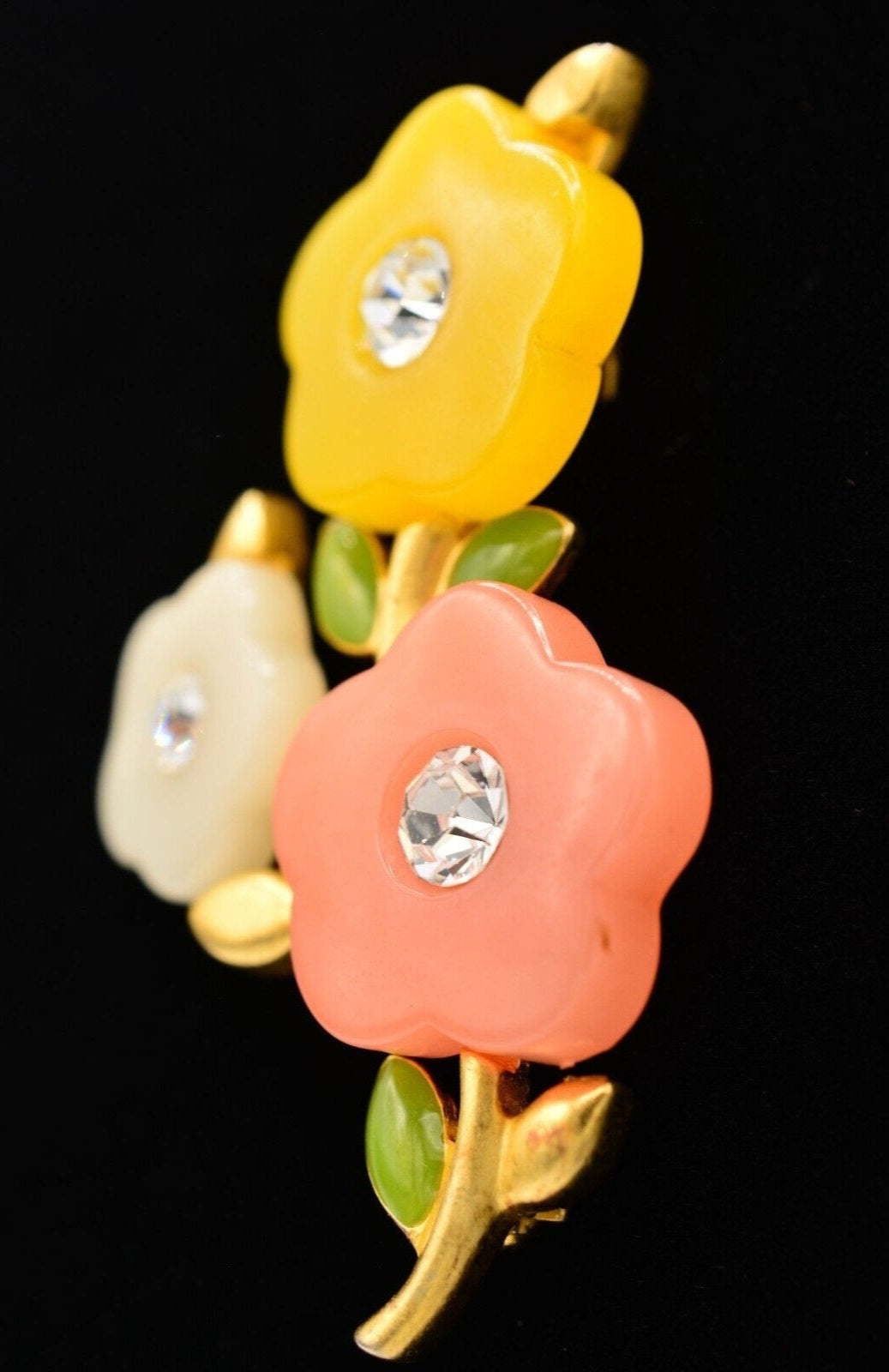 Side view of a vintage Givenchy brushed gold floral brooch with yellow, white, and pink colored acrylic petals with rhinestone crystals in the center on a black background