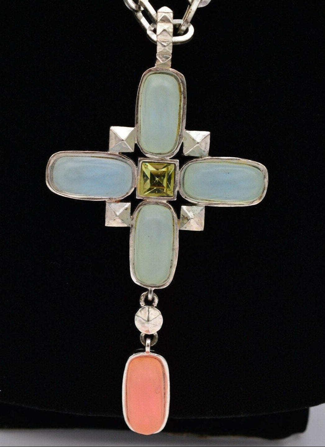 Front view of a vintage Karl Lagerfeld  silver cross pendant with blue and pink frosted glass accents and a vibrant green princess cut rhinestone in the center