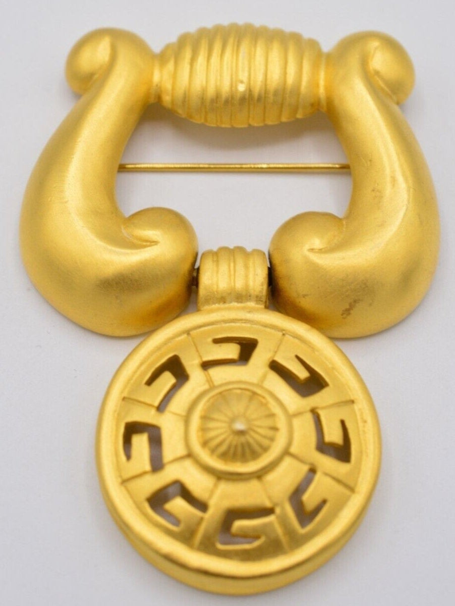Front view of a vintage matte gold Givenchy logo door knocker brooch on a white background