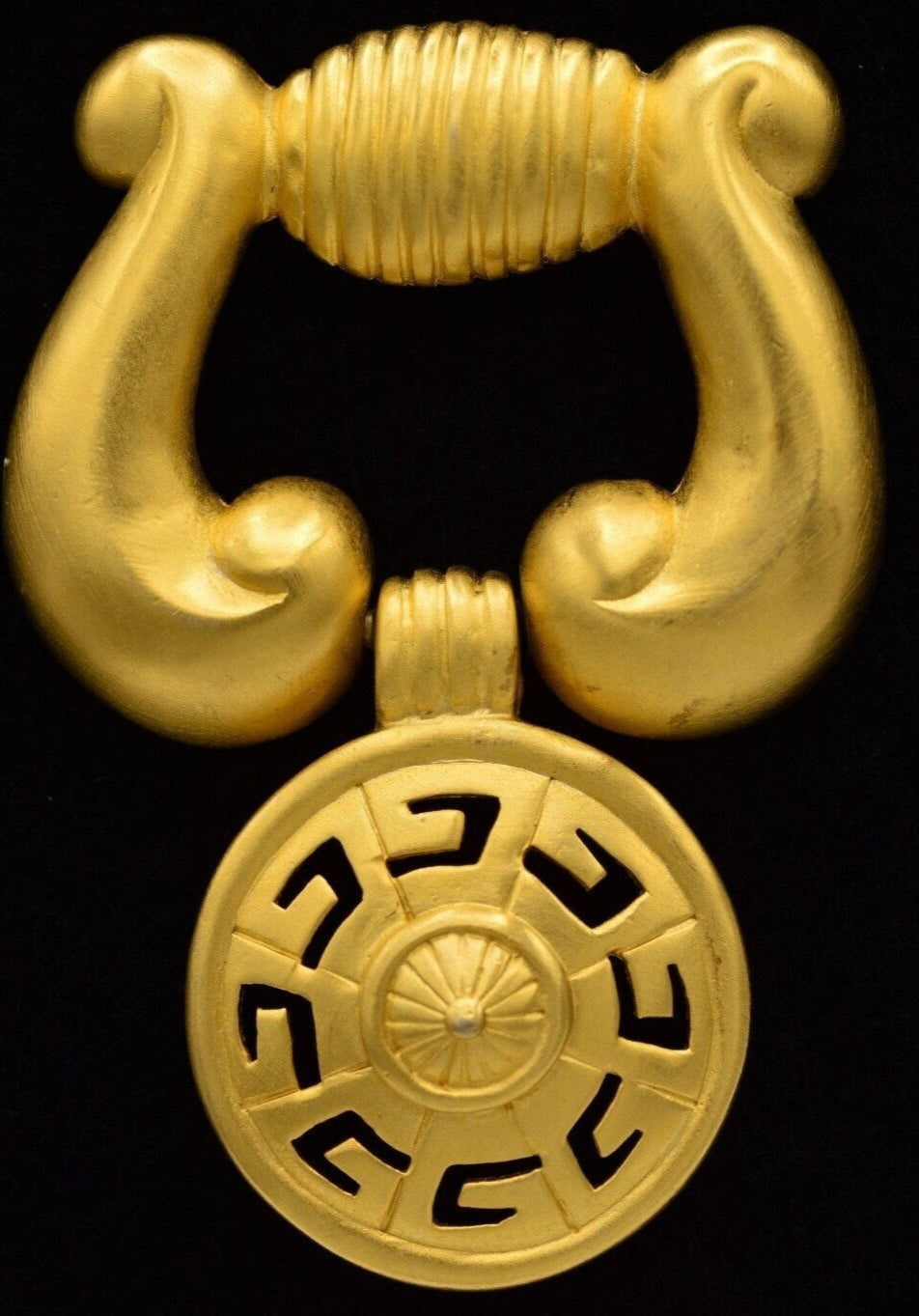 Front view of a vintage matte gold Givenchy logo door knocker brooch on a black background