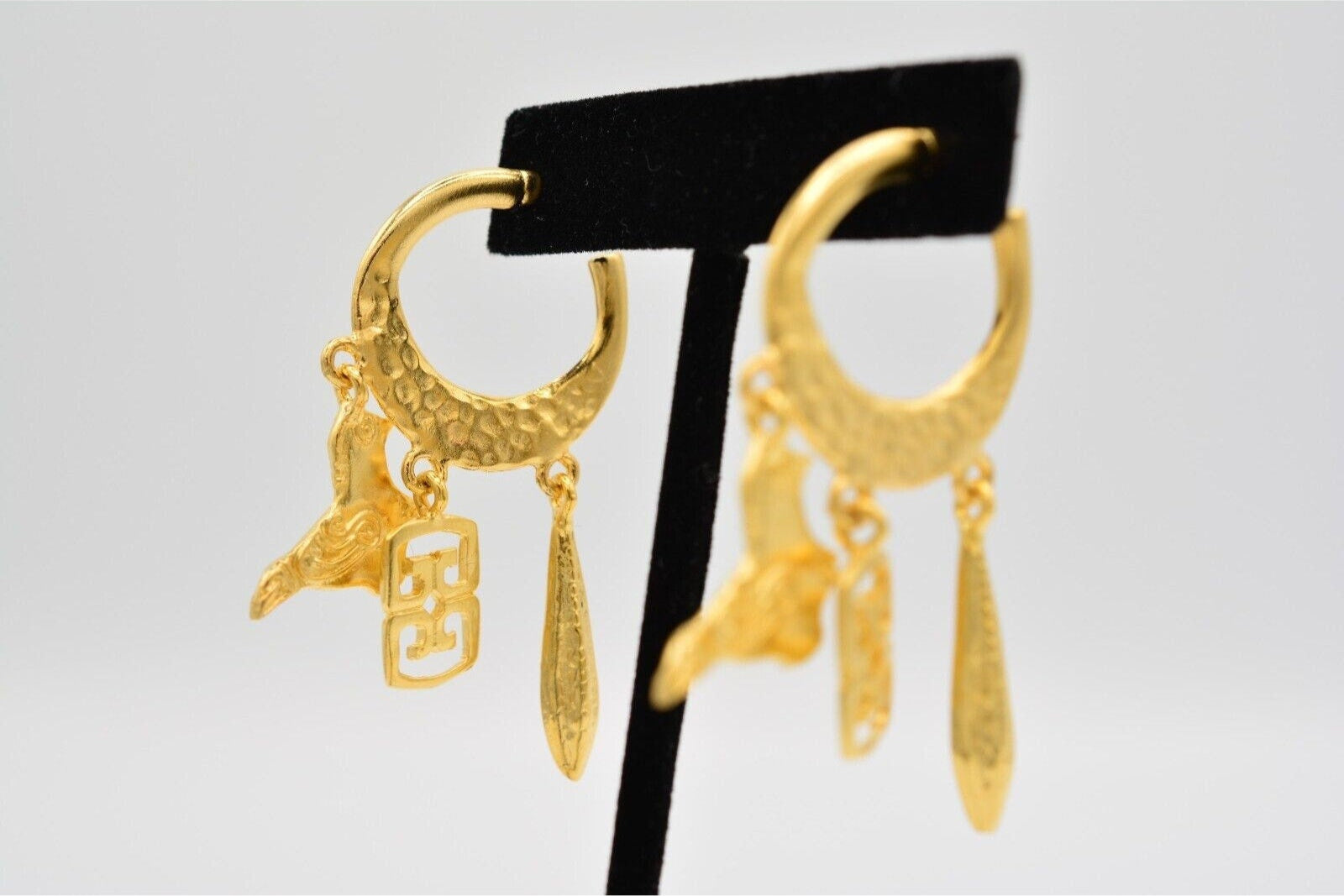 View of vintage matte satin gold pierced earrings on a velvet stand with a bird and other charms dangling