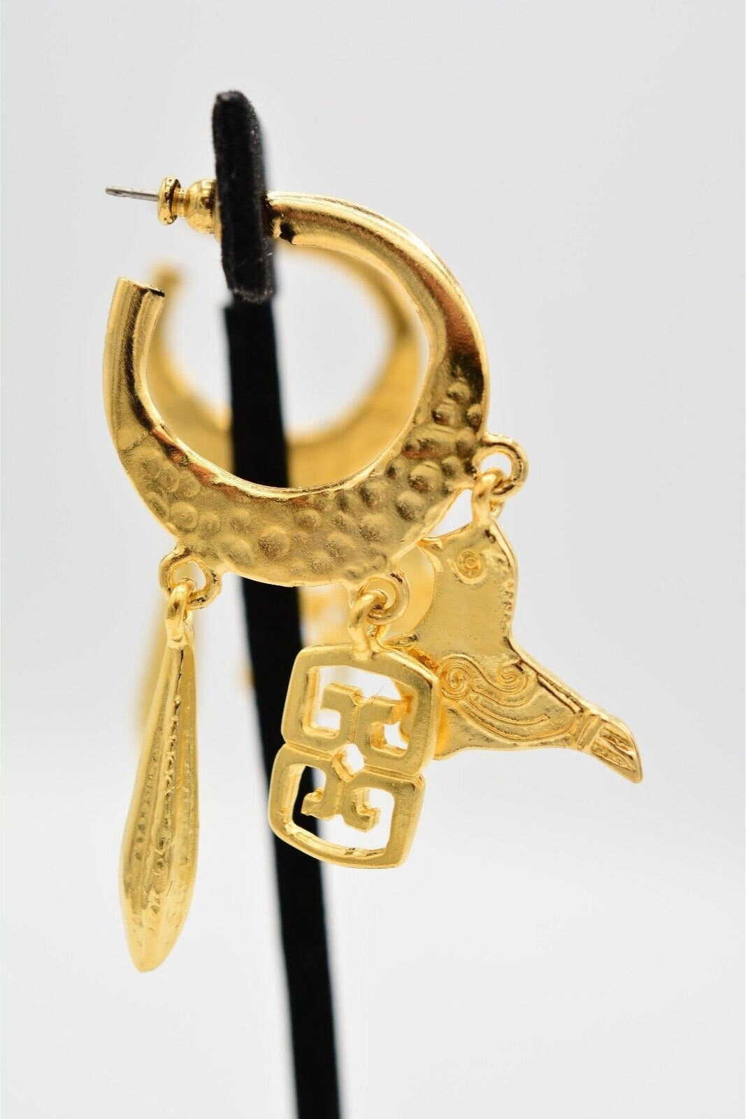 Side view of vintage matte satin gold pierced earrings on a velvet stand with a bird and other charms dangling