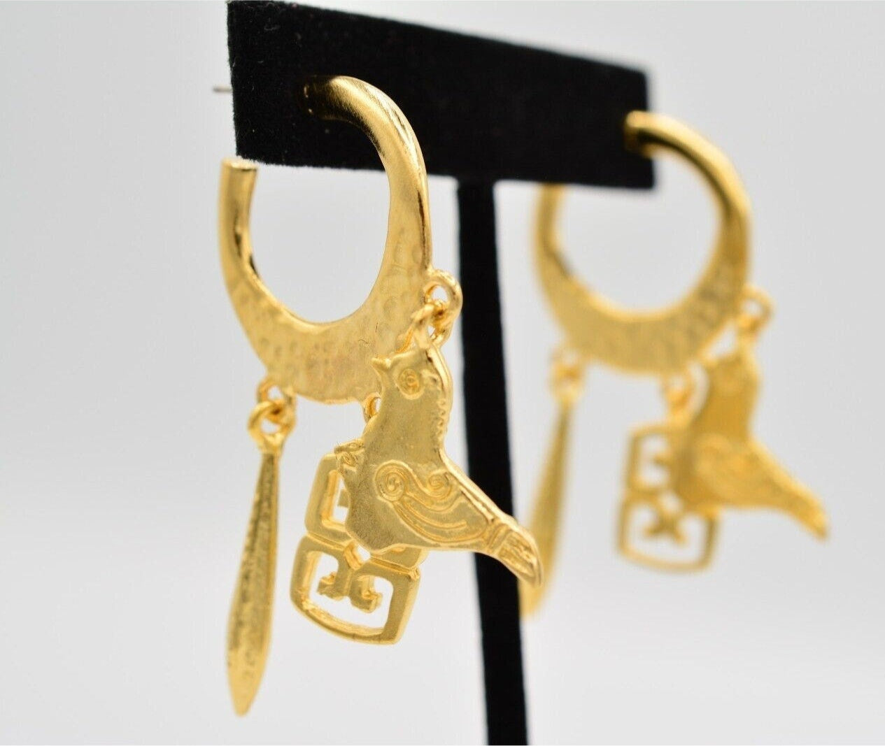 View of vintage matte satin gold pierced earrings on a velvet stand with a bird and other charms dangling