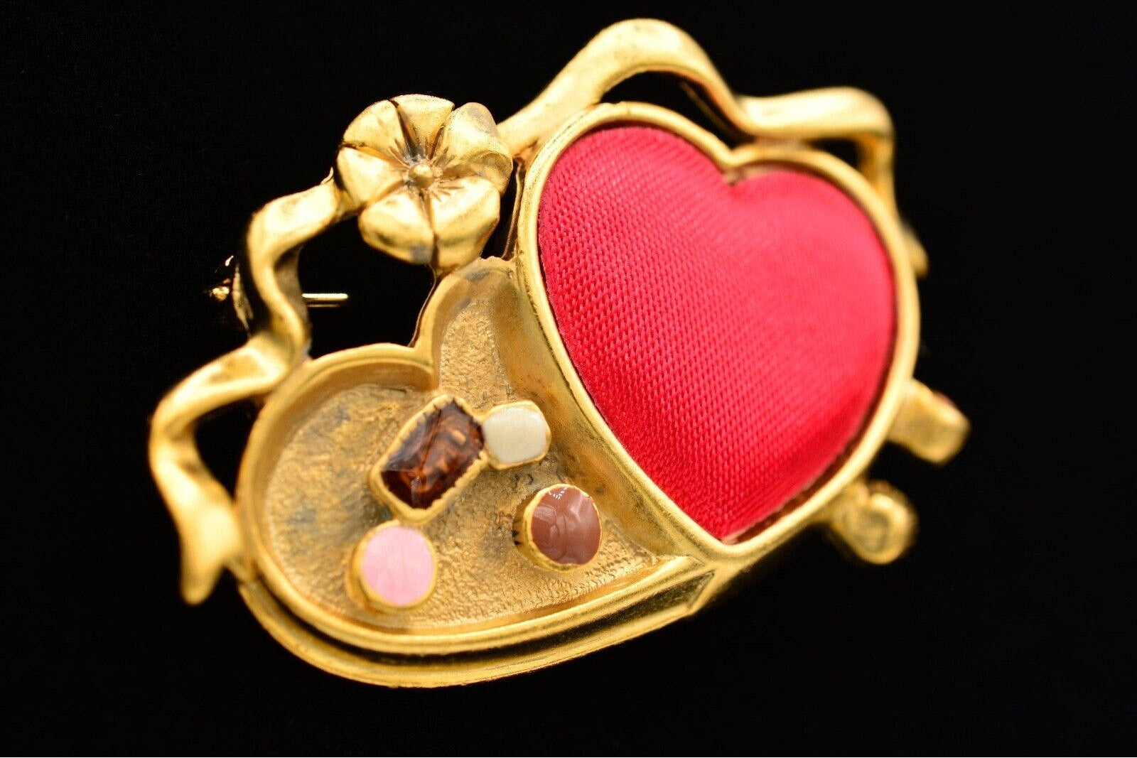 Gold brooch with a red heart and embedded stones on a black background
