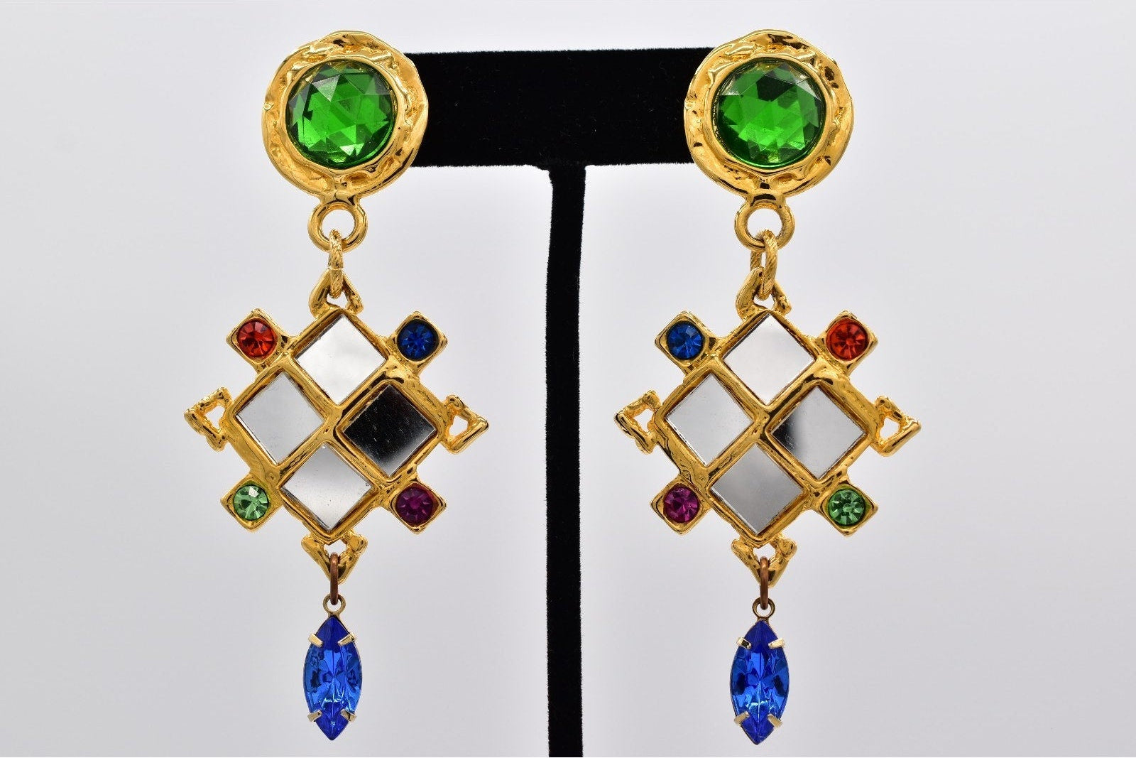 Gold earrings with green, red, and blue gemstones on a white background