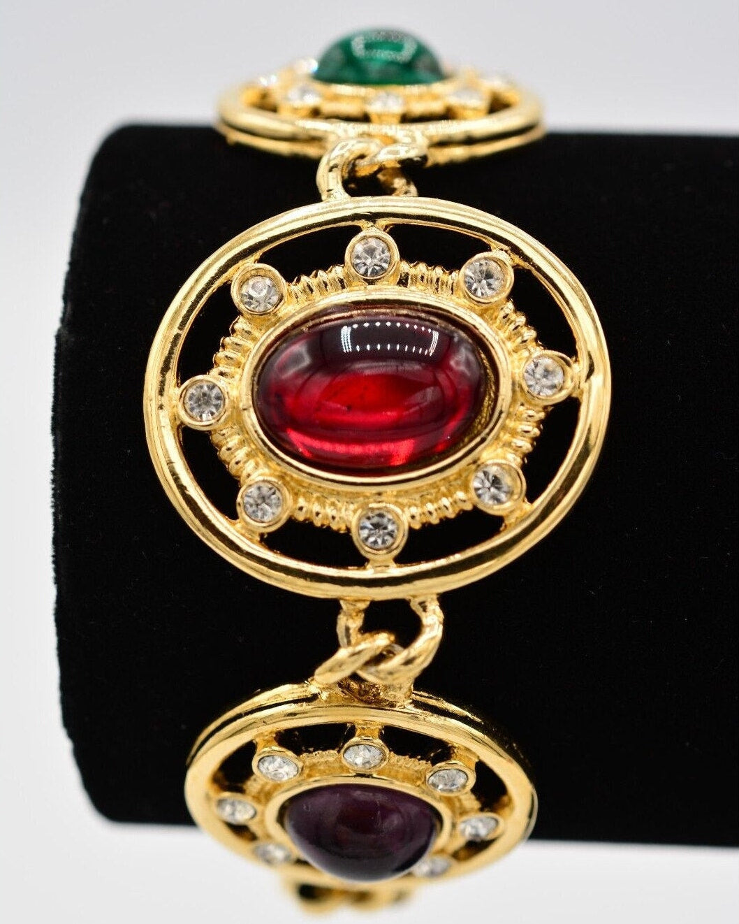 Gold pendant with red and green gemstones on a black stand