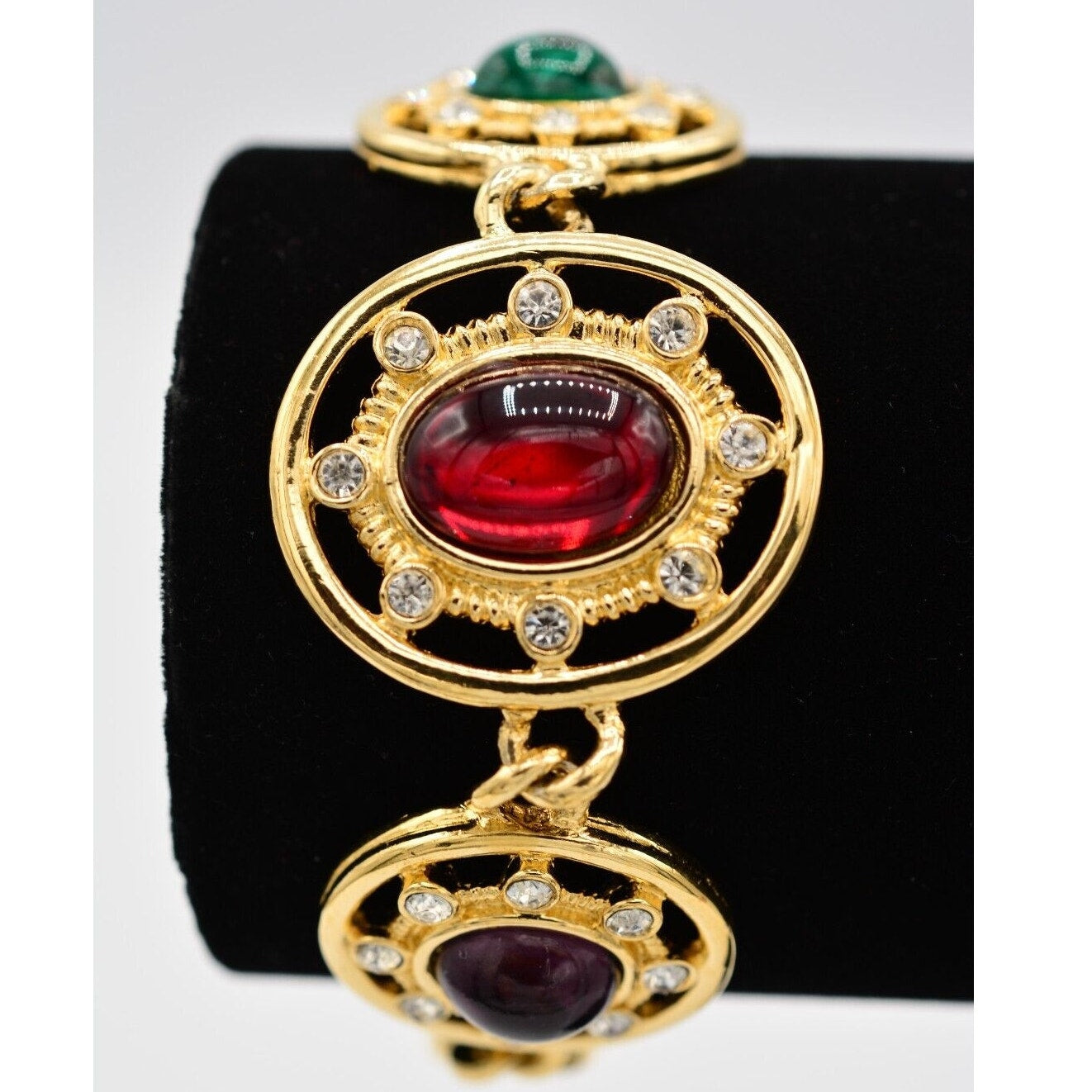 Gold pendant with red and green gemstones on a black stand