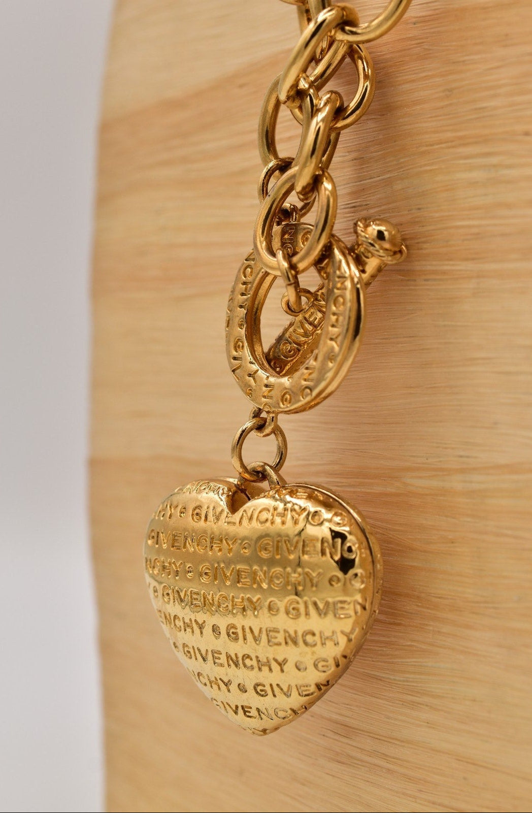 Gold chain with a heart-shaped Givenchy charm on a wooden surface