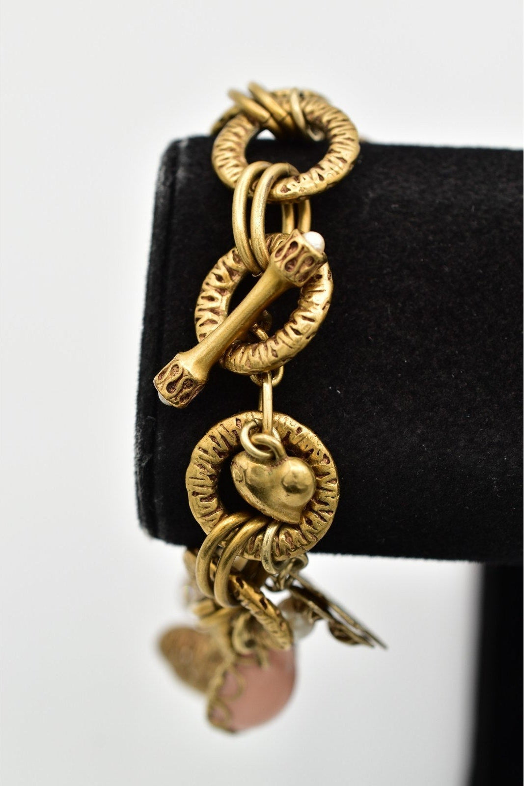 Gold chain earring with heart charm on a black stand against a white background