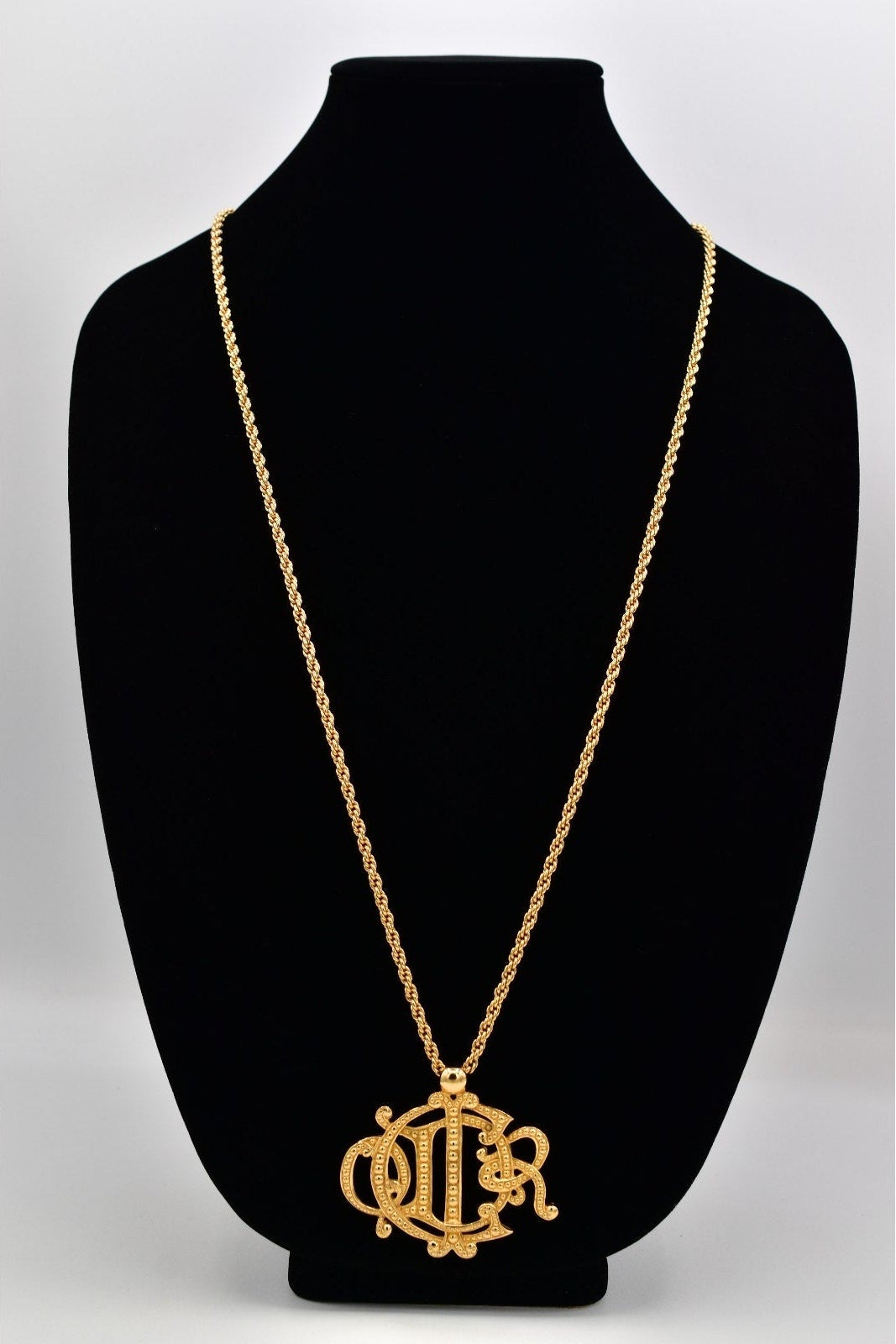 Gold necklace with a pendant on a black mannequin bust against a white background