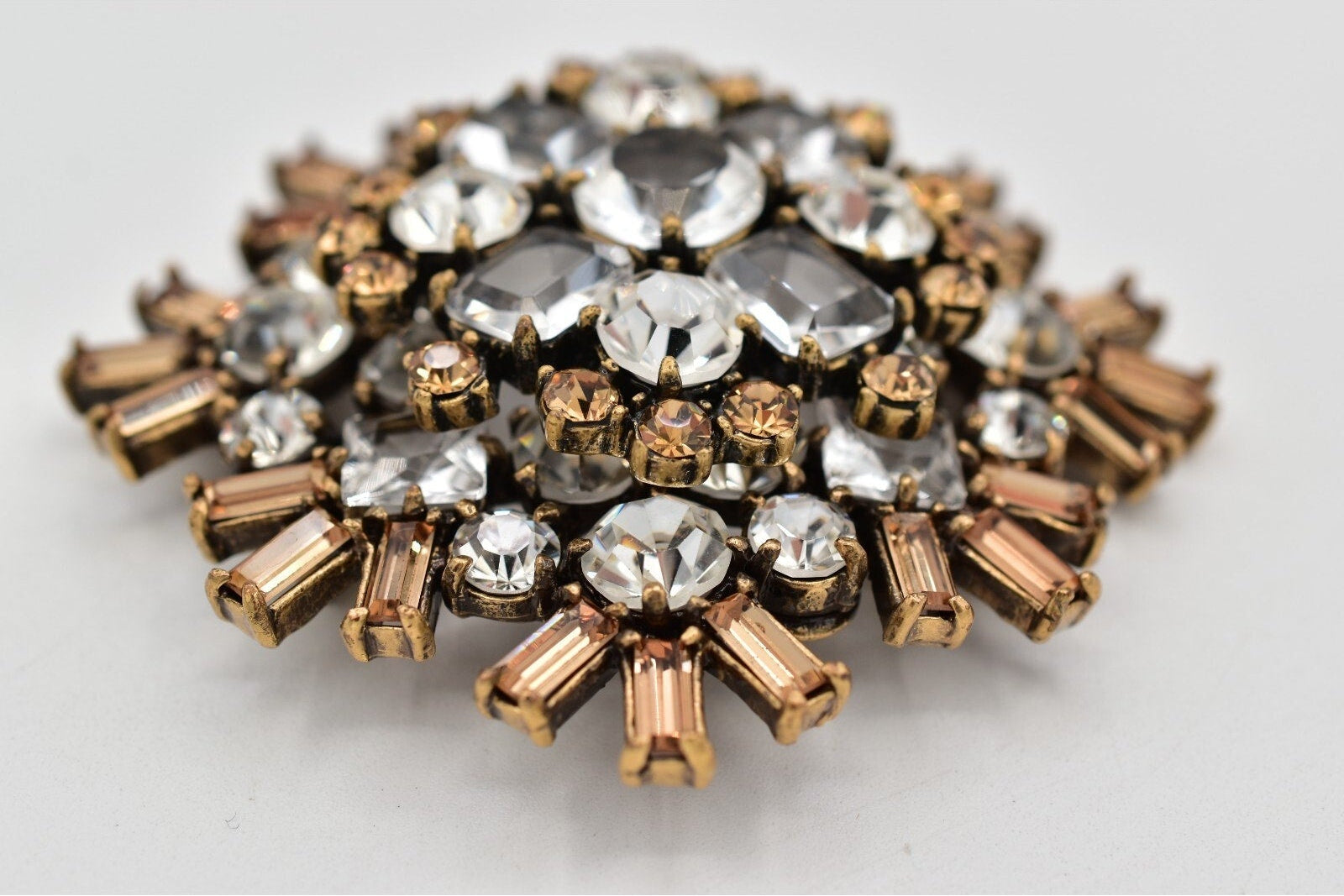 Decorative brooch with gold and clear gemstones on a light gray background