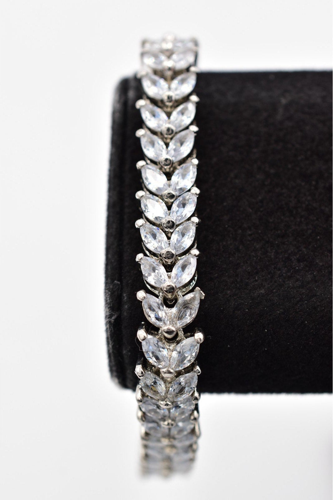 Silver bracelet with clear stones on a black stand against a white background