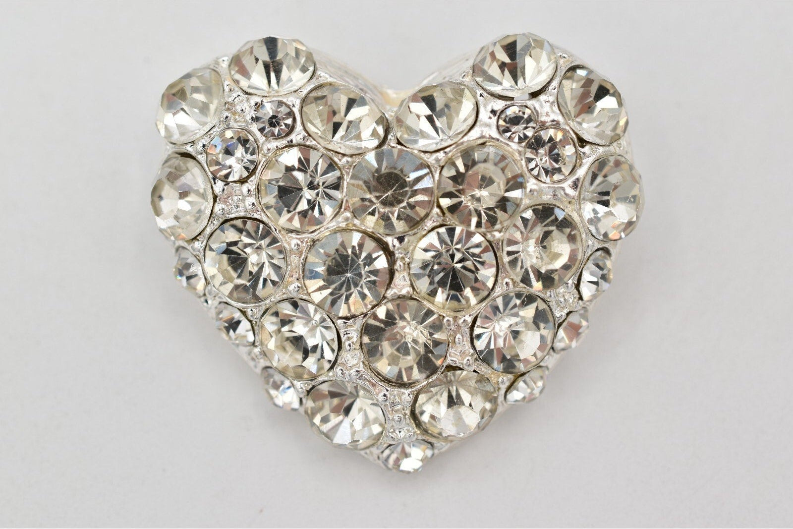 Heart-shaped decorative item with crystal-like stones on a light gray background