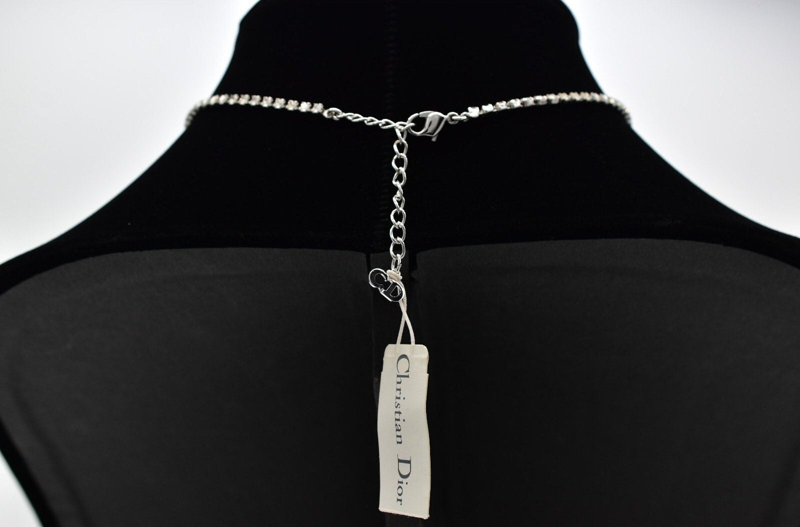 Silver necklace with a Christian Dior tag on a black mannequin against a white background