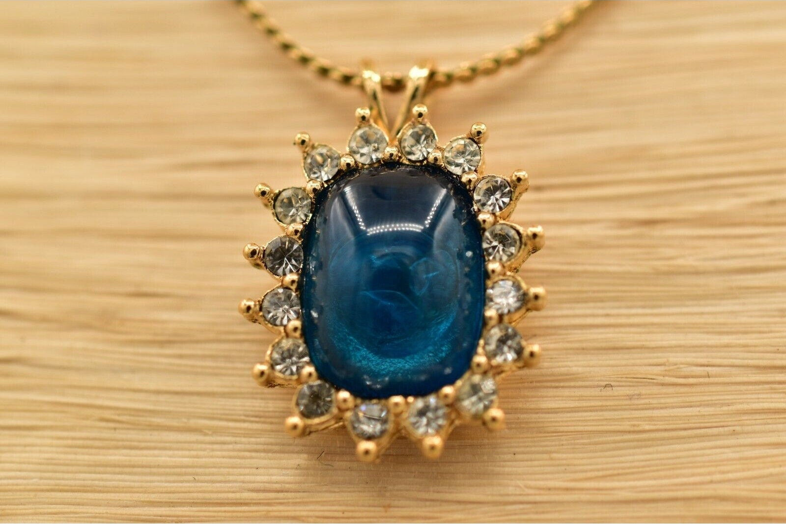 Gold necklace with a blue gemstone pendant on a wooden surface