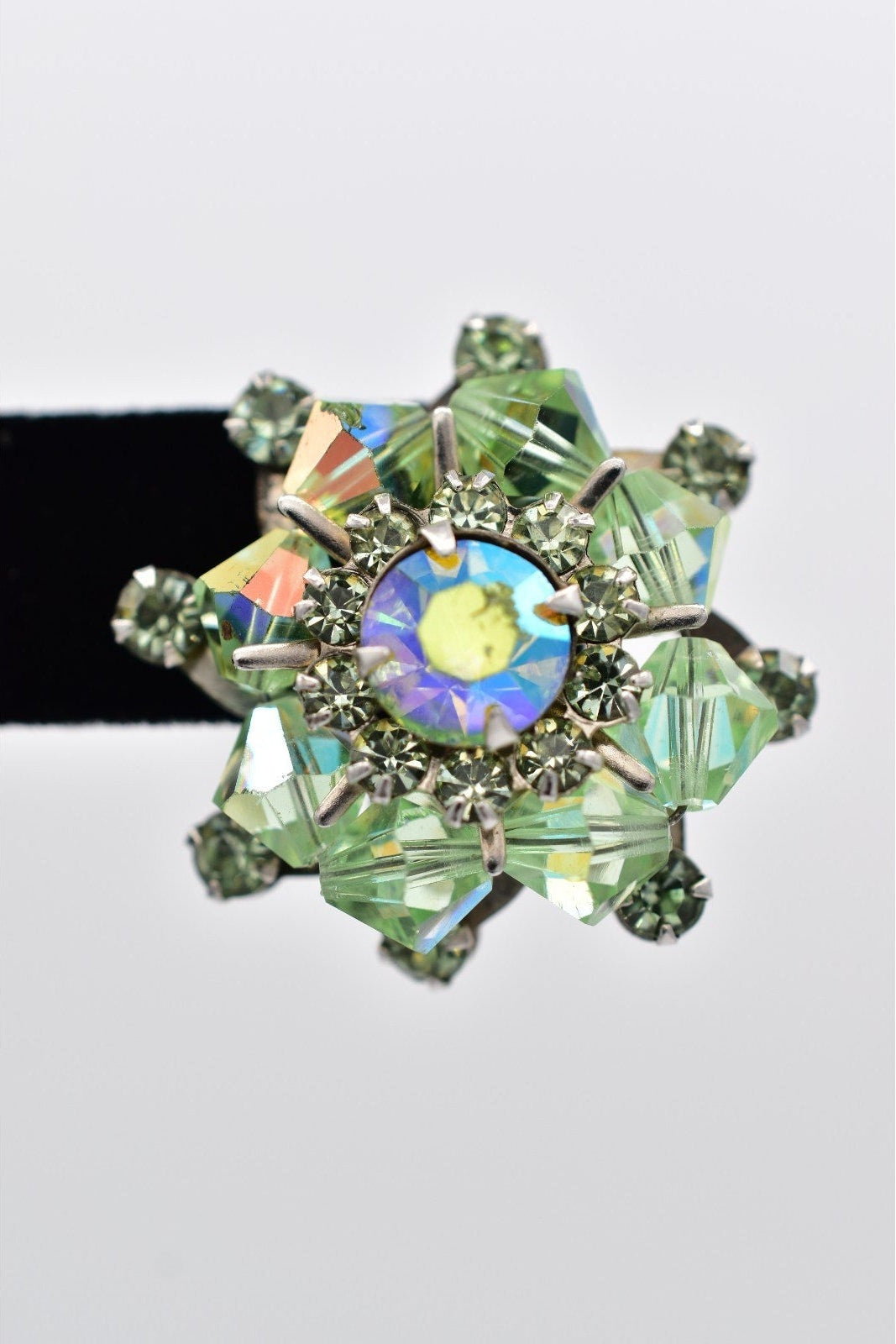 Decorative brooch with green gemstones and a colorful center on a white background