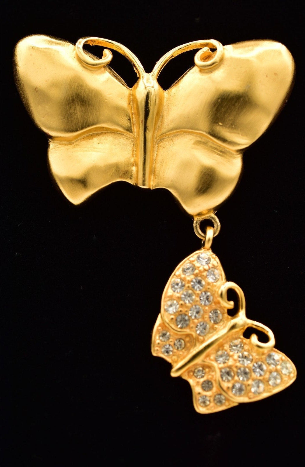 Gold butterfly brooch with a smaller butterfly pendant on a black background
