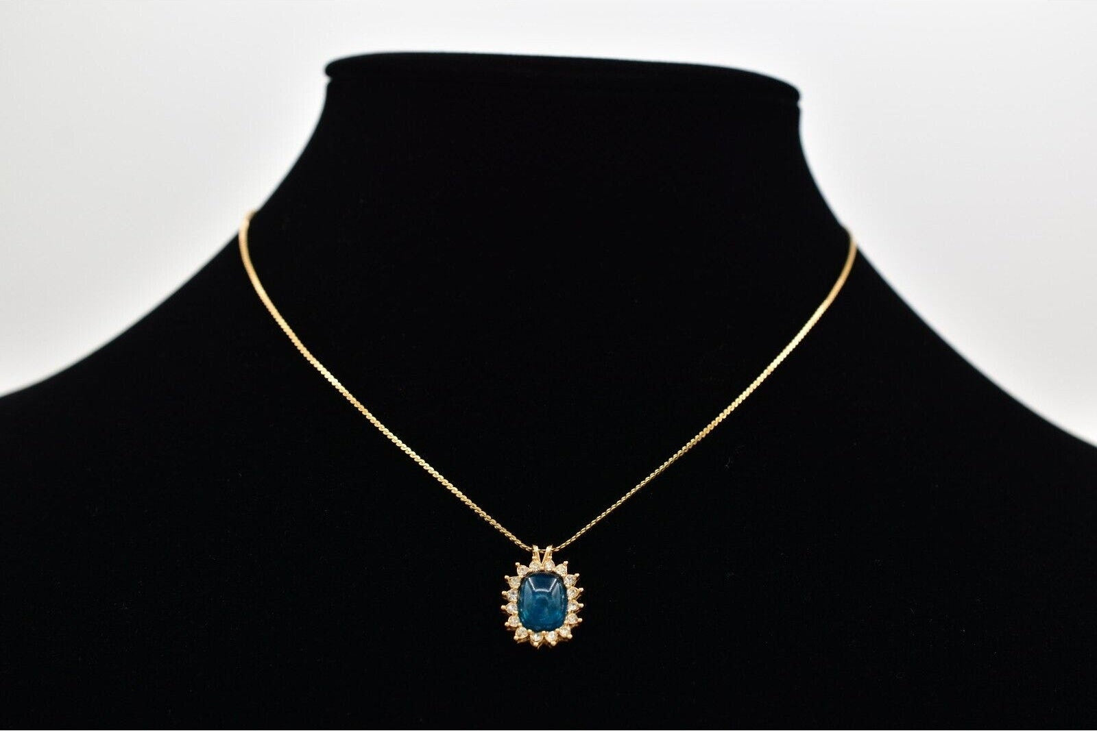 Gold necklace with a blue pendant on a black mannequin against a white background