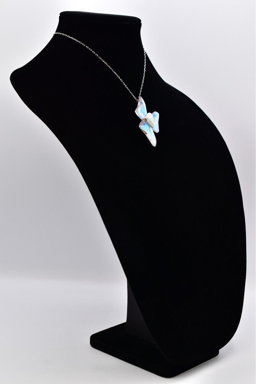 A silver necklace with a butterfly-shaped pendant featuring light blue and white inlay details, displayed on a black jewelry bust against a light gray background.