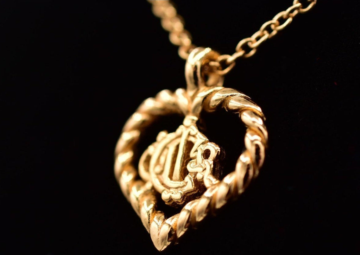 Gold heart-shaped Christian Dior monogram pendant on a black background