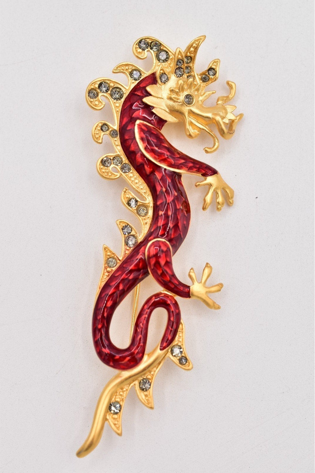 Decorative lizard-shaped brooch with red body and gold outline on a white background
