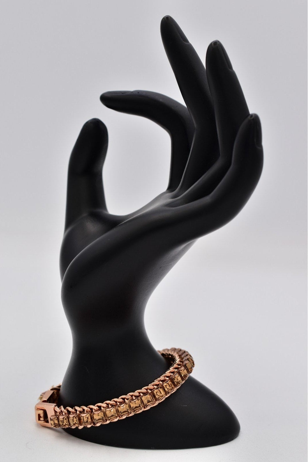 Black mannequin hand holding a brown bracelet on a gray background