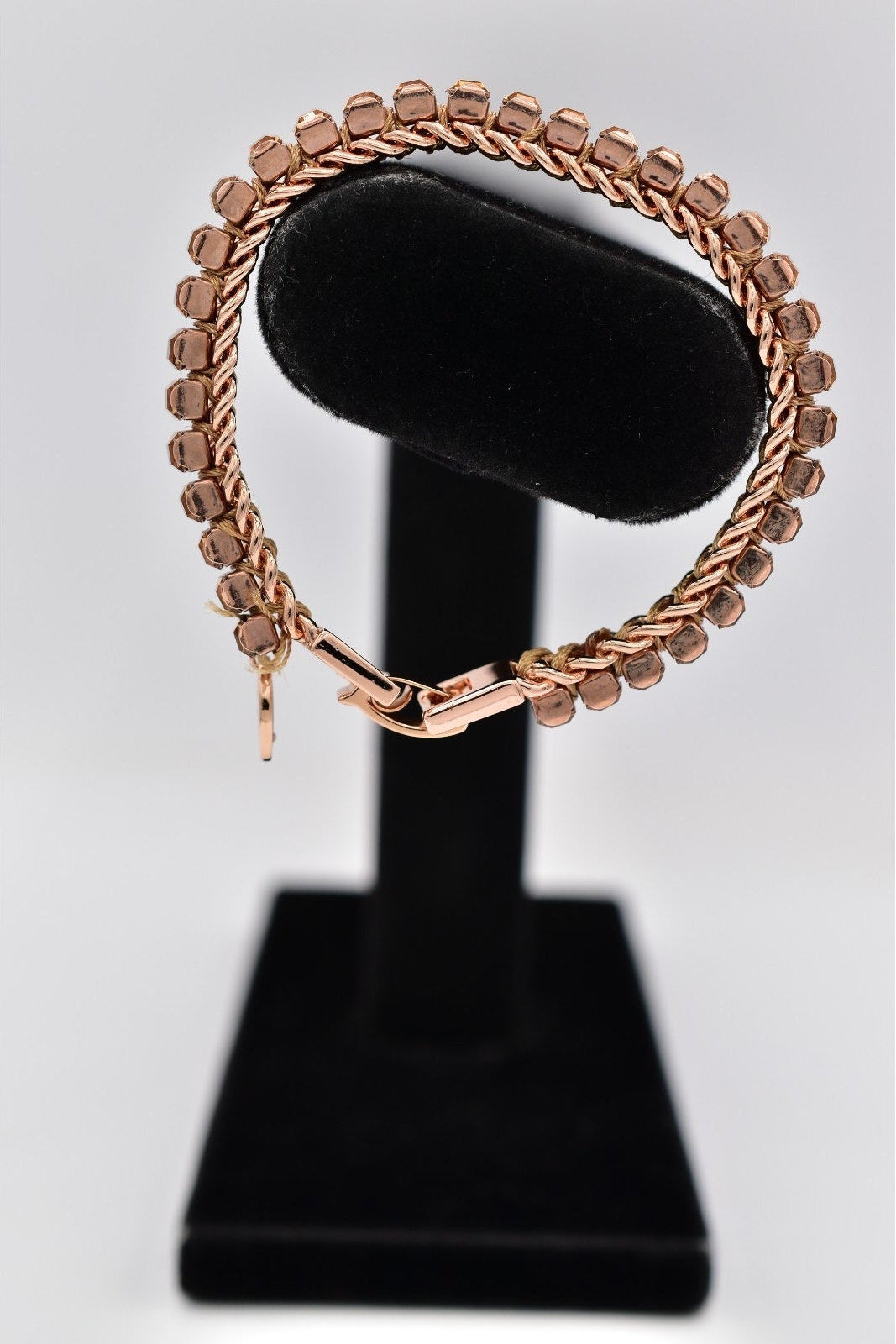 Rose gold bracelet on a black stand against a white background