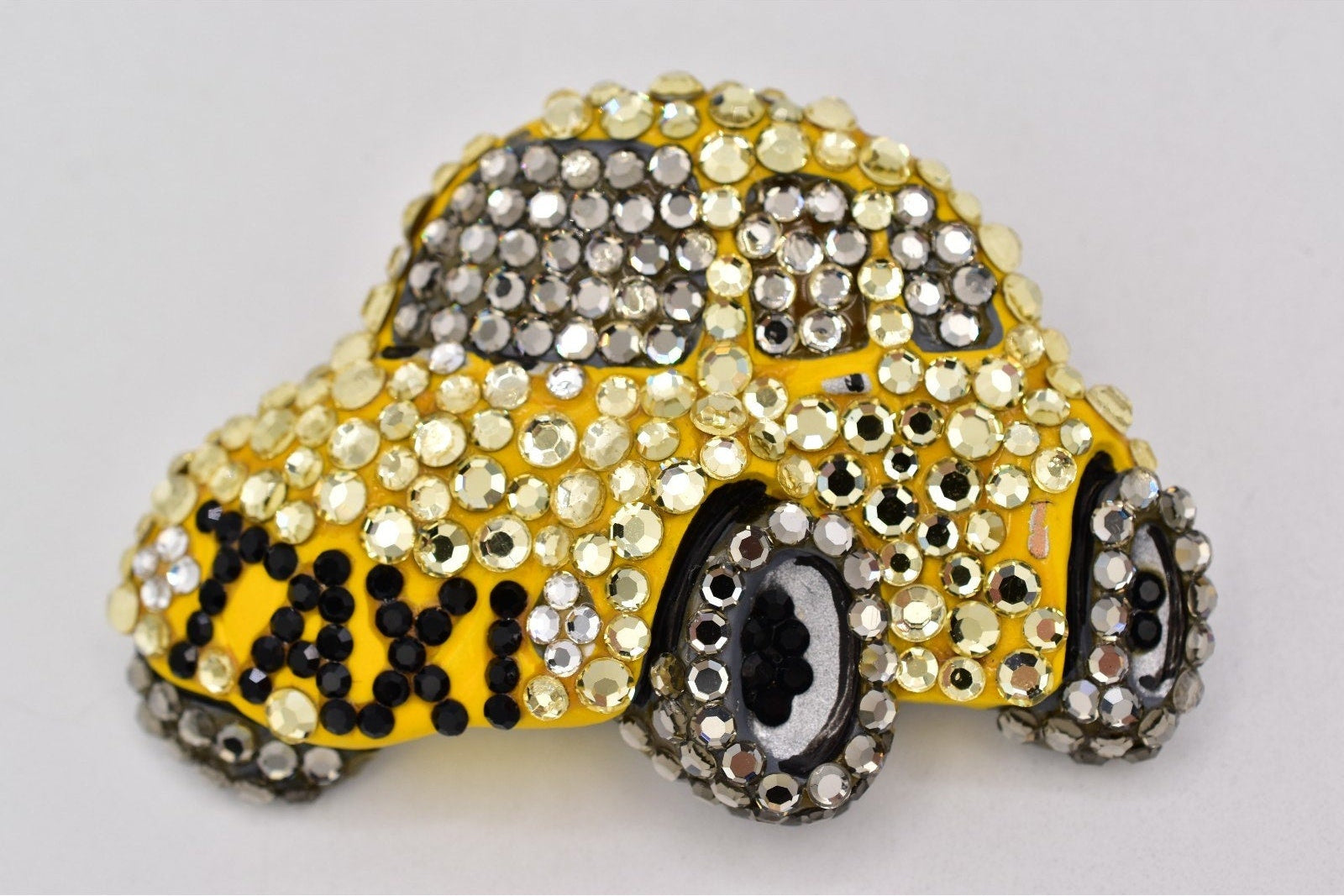 Decorative brooch shaped like a yellow taxi with rhinestone embellishments on a white background