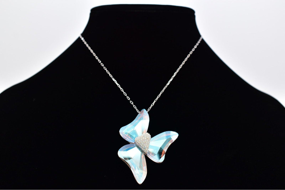 A silver-tone chain necklace with a butterfly-shaped pendant made of iridescent light blue crystals, displayed on a black jewelry bust against a white background.