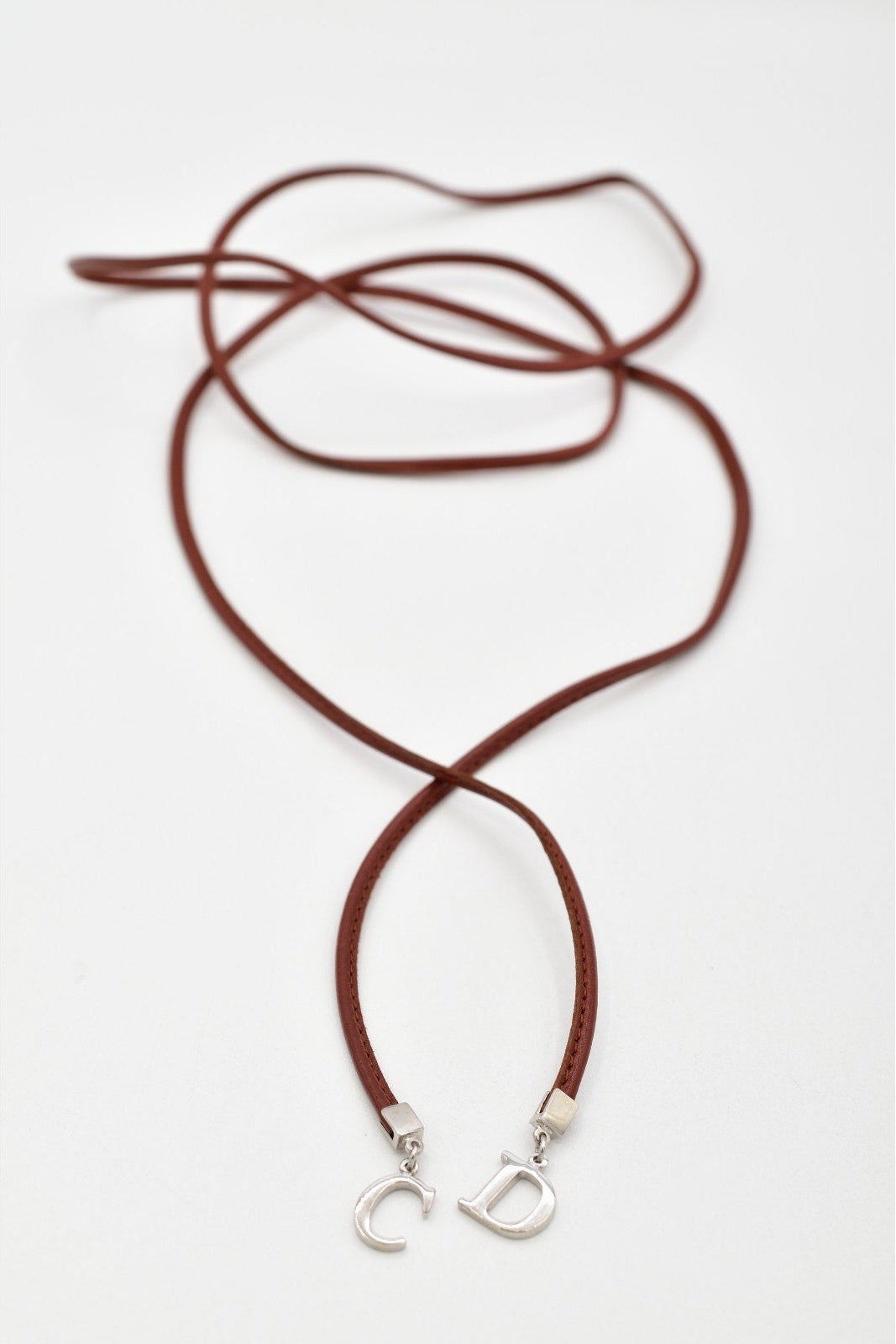 A dark brown leather cord necklace with silver-toned metal letter charms spelling 'CD', displayed on a clean white background.