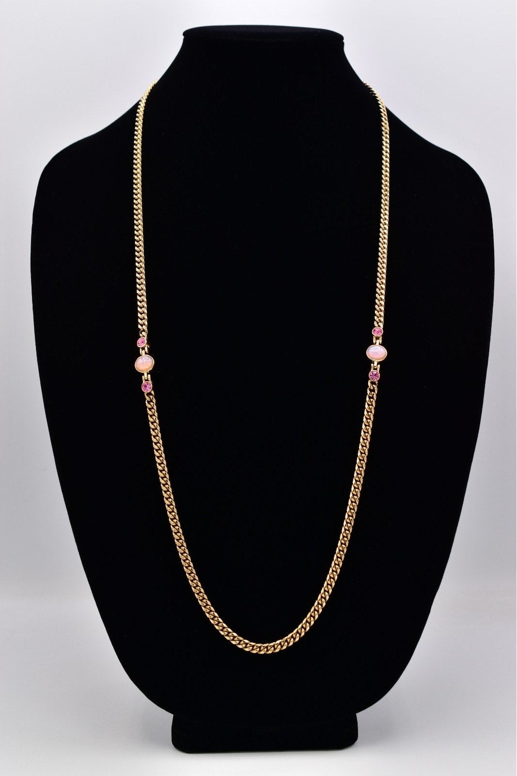 A gold-toned chain necklace with two small pink bead accents, displayed on a black velvet jewelry bust against a light gray background.