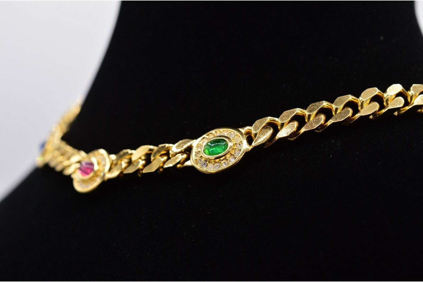 Gold necklace with gemstone accents on a black mannequin.

