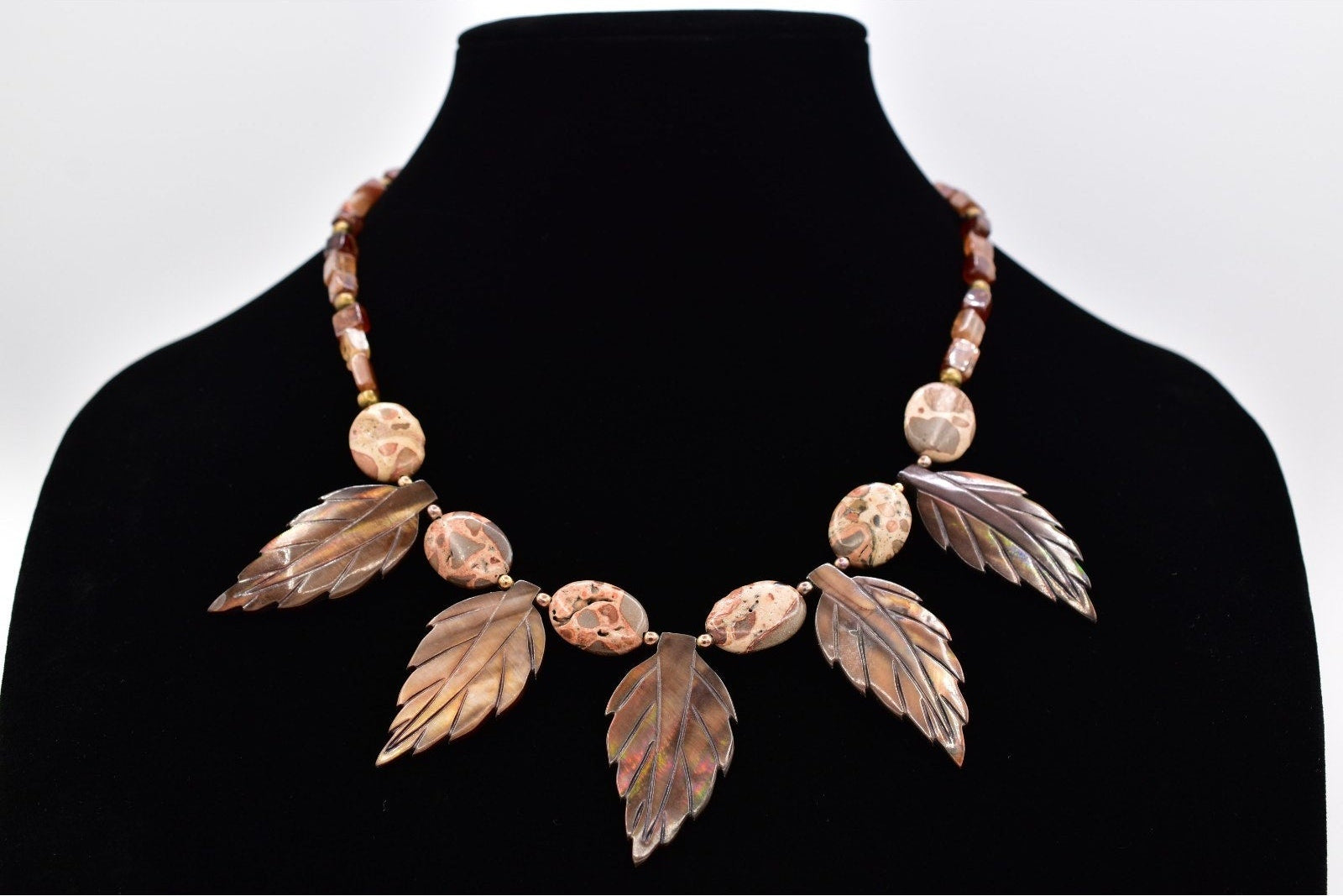 Necklace with leaf-like designs on a black mannequin against a white background