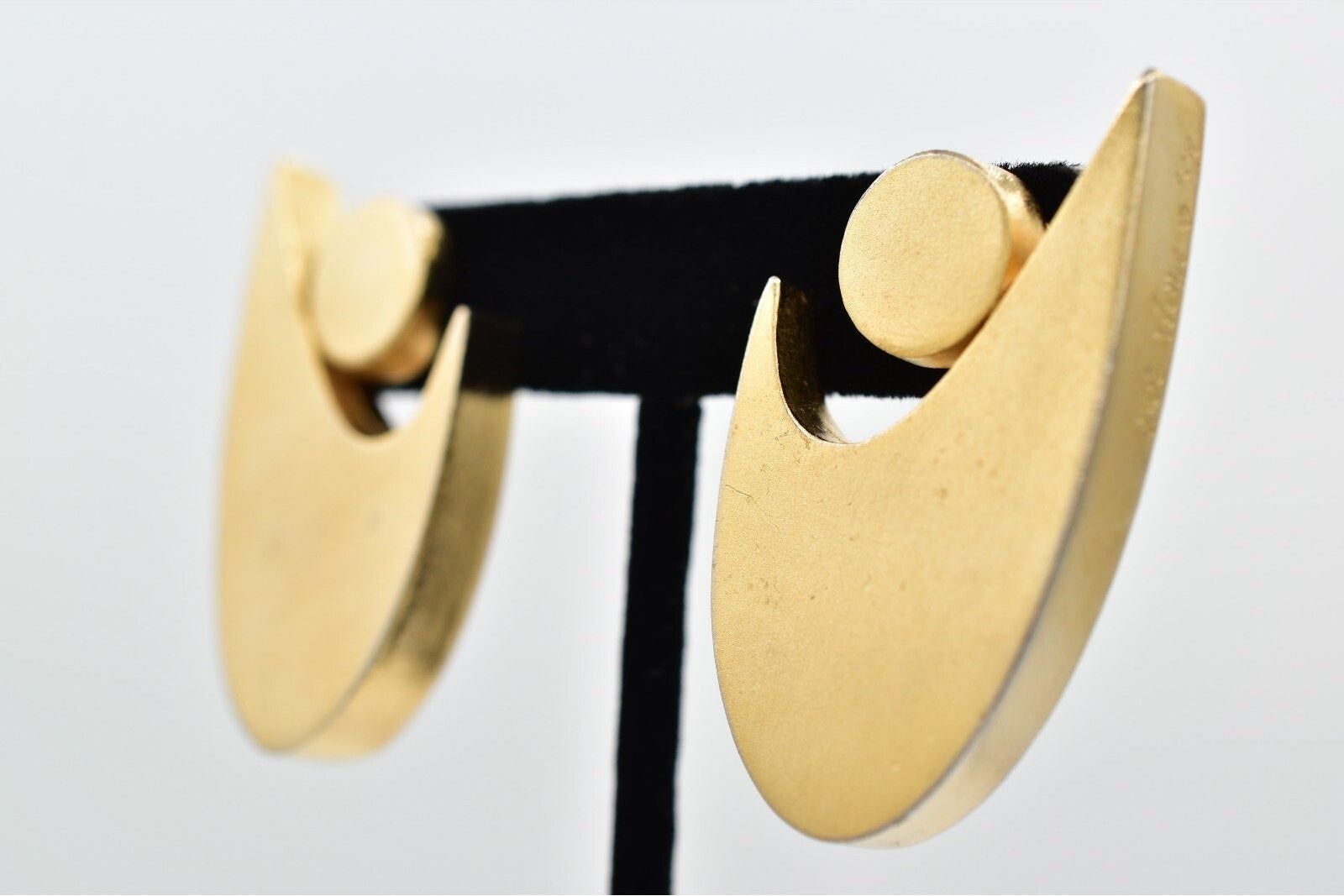 Gold earrings on a stand against a light gray background