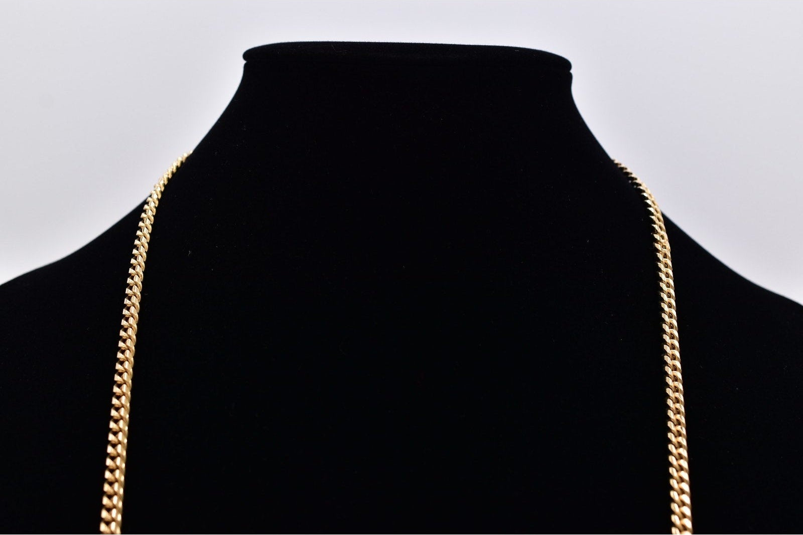 A gold chain necklace displayed on a black velvet neck bust against a light gray background.