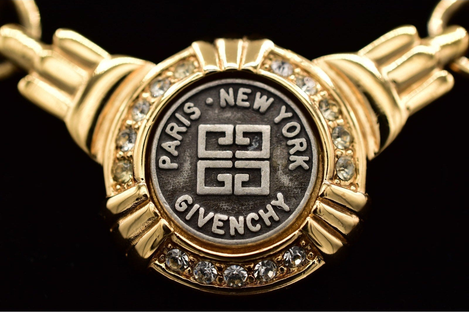 Gold bracelet with Givenchy logo and 'Paris New York' text on a black background