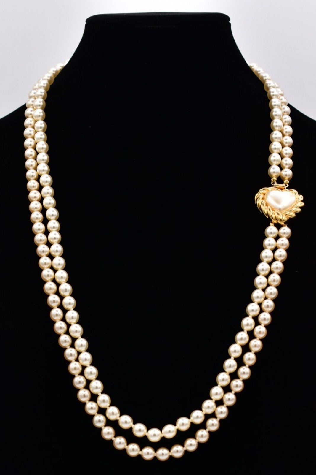 Pearl necklace with a gold clasp on a black mannequin against a white background