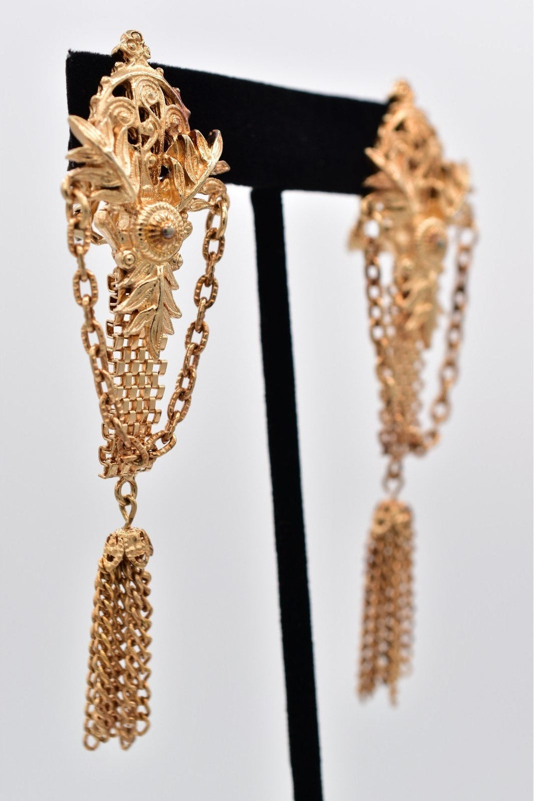 Gold chain earrings on a black stand against a white background