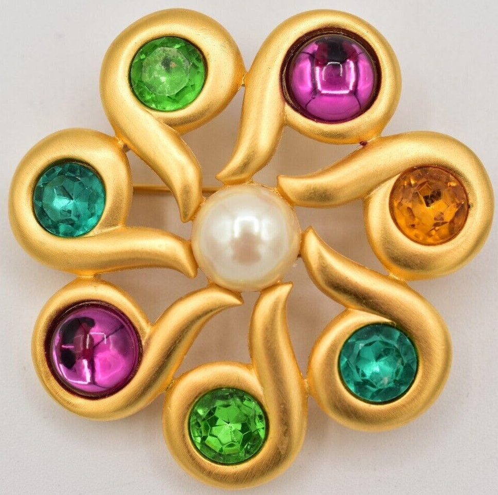 A vintage Givenchy flower brooch with bright crystals and a gold finish on a white background.