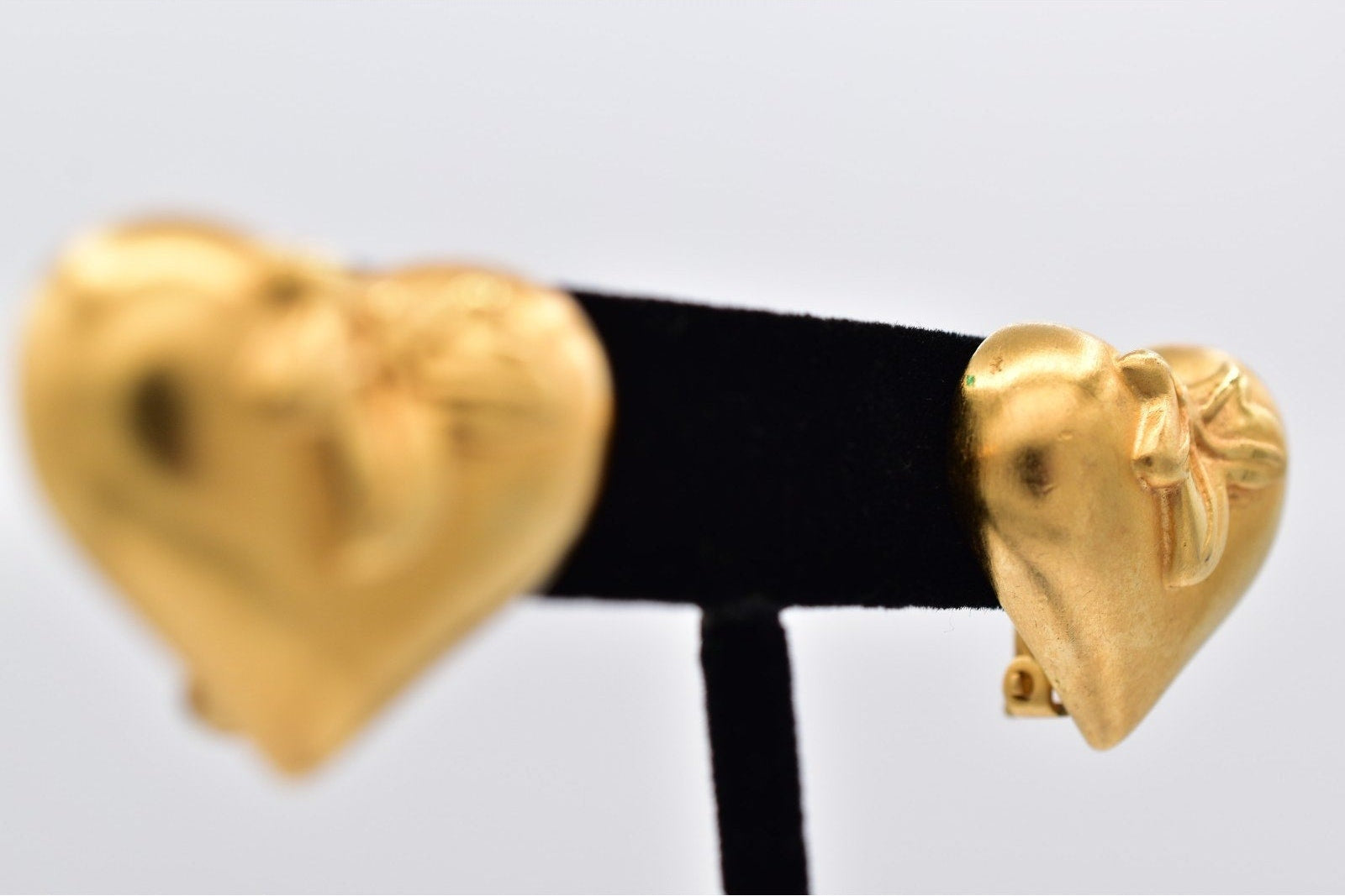 Gold heart-shaped earrings on a black stand against a light gray background