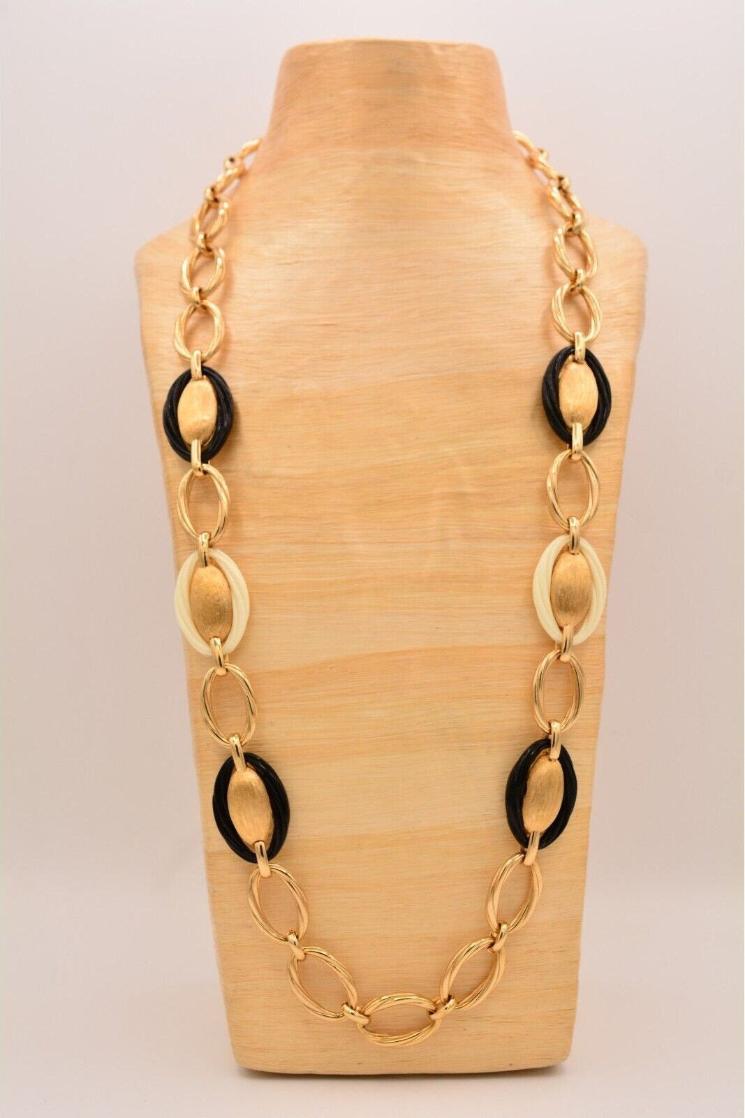 Gold chain necklace with black accents on a wooden mannequin bust.