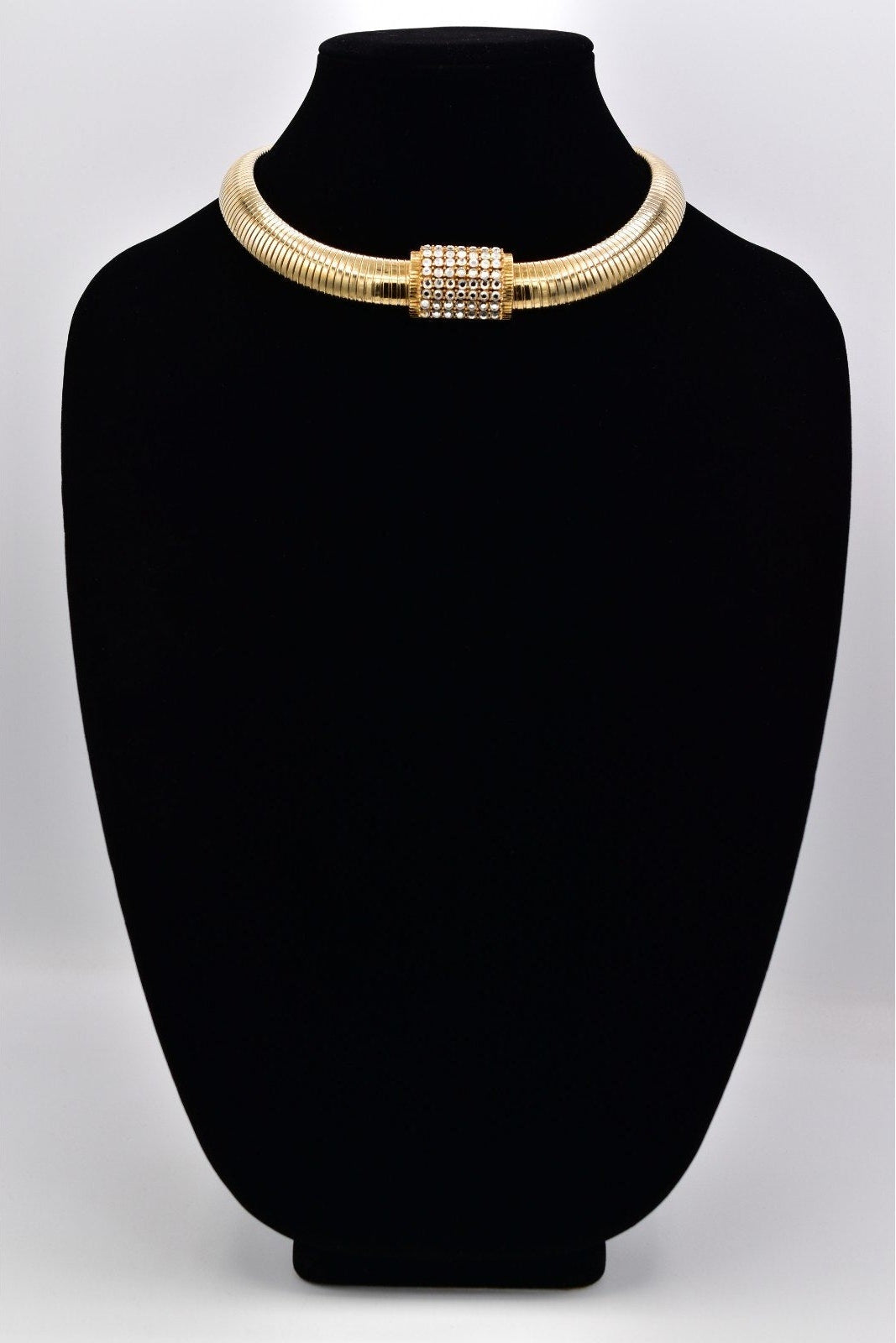 Gold necklace on a black mannequin bust against a light gray background