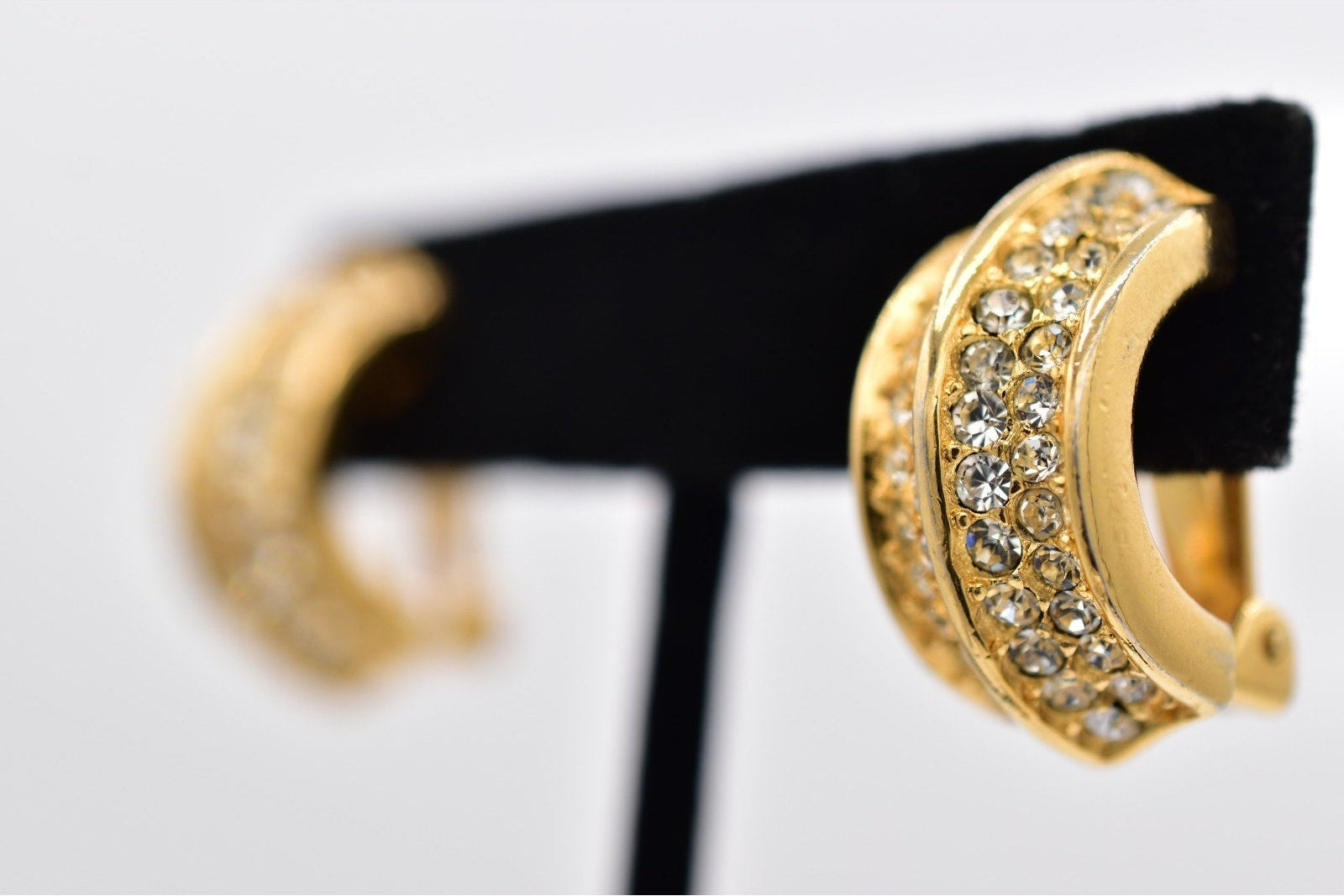 Gold hoop earrings with embedded stones on a black stand against a white background