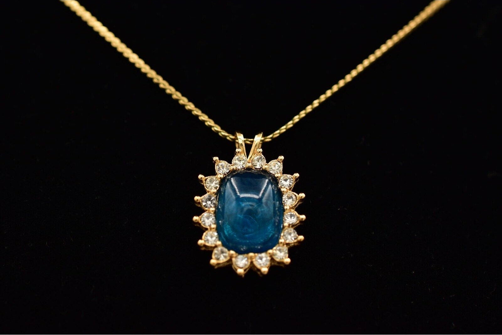 Gold necklace with a blue gemstone pendant on a black background