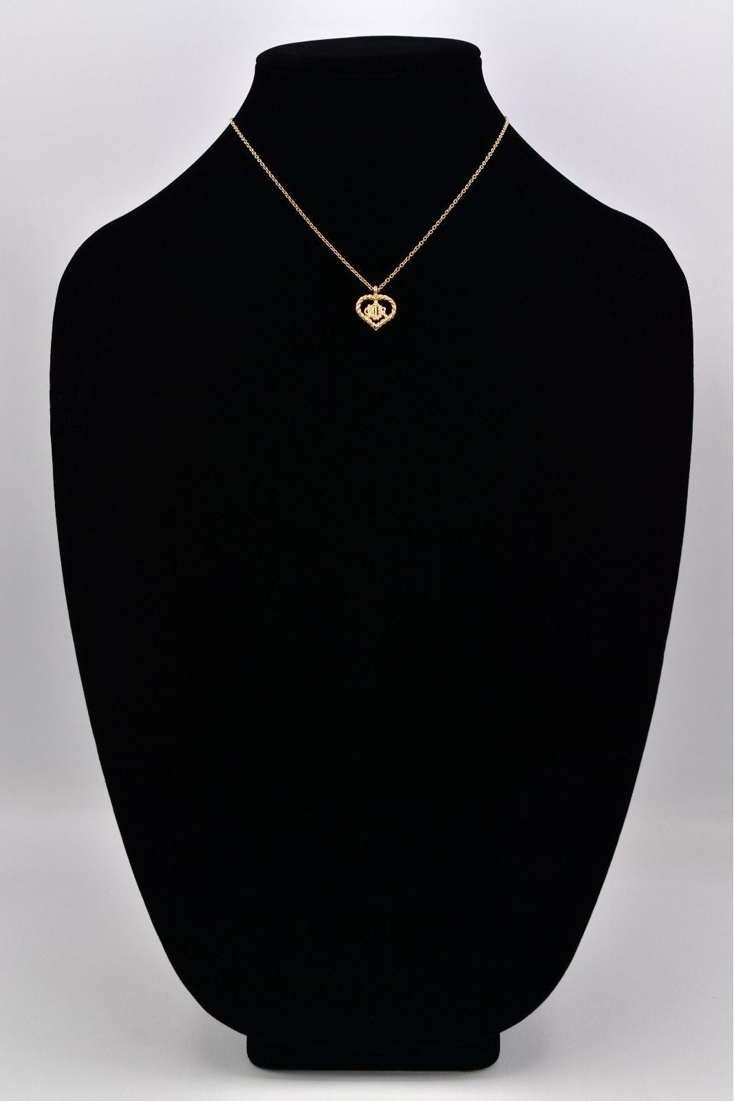 Gold necklace with a heart-shaped pendant on a black mannequin bust against a white background