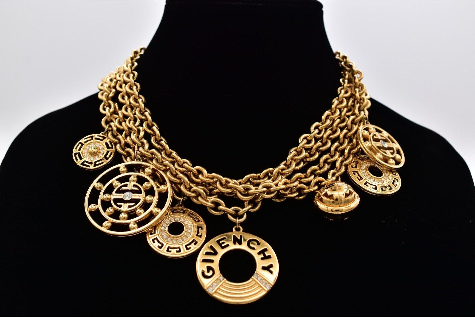 Gold necklace with various pendants on a black mannequin against a white background