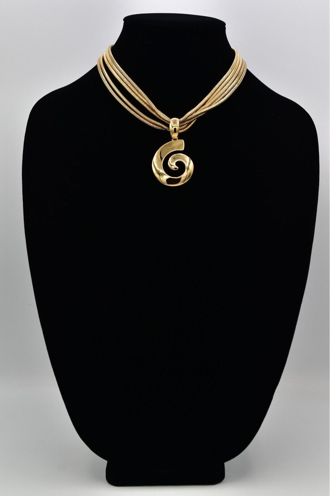 Gold necklace with a spiral pendant on a black mannequin bust against a gray background