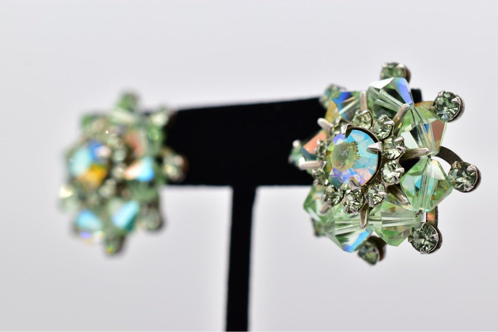 Pair of green gemstone earrings on a black stand against a light gray background