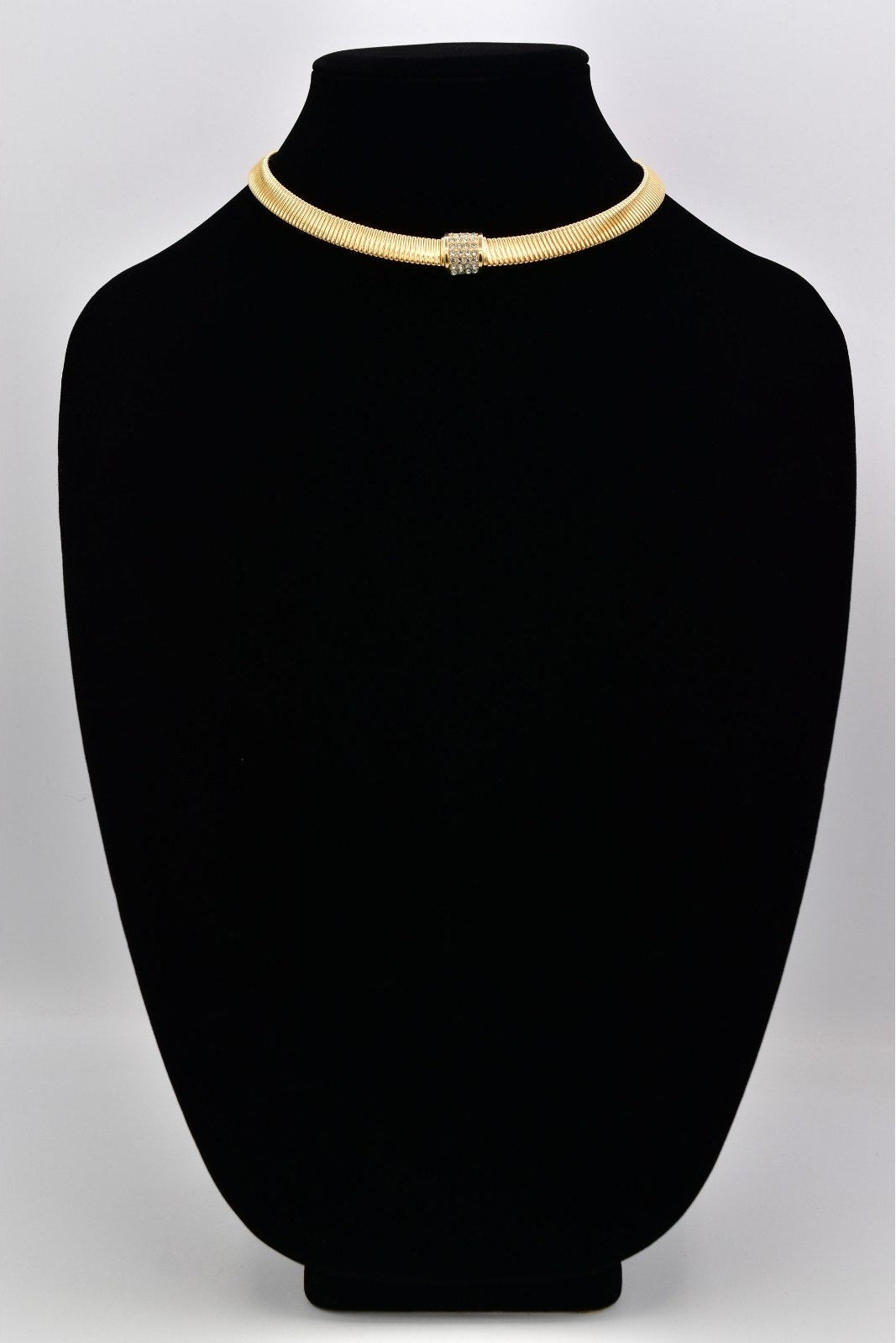Gold necklace on a black mannequin bust against a white background